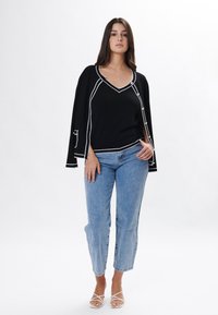 Top negro con ribetes blancos, diseño de cuello en V y mangas sueltas; combinado con jeans de mezclilla claros y sandalias blancas con tiras.