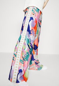Pantalones de pierna ancha coloridos que presentan un vibrante patrón abstracto en múltiples colores. Incluye una franja lateral blanca con acentos de logo dorado.