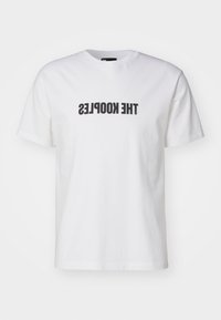 Bílé bavlněné tričko s krátkým rukávem, na přední straně s výrazným černým inverzním potiskem "THE KOOPLES". Klasický design s kulatým výstřihem.