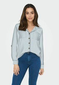 Light blue and white striped button-up shirt with two chest pockets, long sleeves, and brown buttons, paired with blue denim jeans.