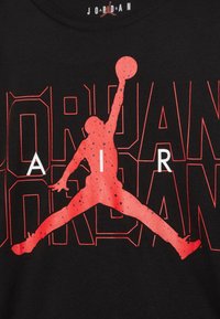 Černé tričko s velkým červeným siluetem skákající postavy držící basketbal, s tučným červeným a bílým nápisem "JORDAN AIR."