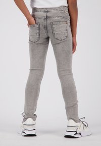 Jeans skinnies de mezclilla gris con un diseño desgastado, dos bolsillos traseros y una cintura de altura media, combinados con zapatillas blancas.