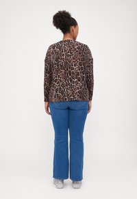 Top s leopardím potiskem, dlouhé rukávy, volný střih, detail zadního švu; kombinováno s modrými zvonovými džíny a světle šedými teniskami.