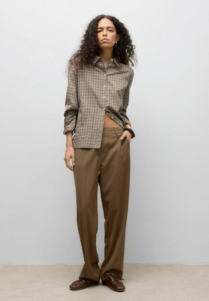 Camicia a quadri marroni con bottoni e maniche lunghe, abbinata a pantaloni brown a vita alta, larghi e testurizzati e scarpe marroni con lacci.