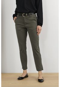 Pantalon en coton vert olive avec une coupe slim, comportant des poches avant et des ourlets roulés, associé à des ballerines noires et un top noir à manches longues.