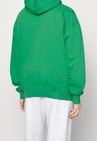 Felpa verde con cappuccio dal taglio morbido, con polsini e orlo a costine. Il tessuto ha una texture liscia, mostrata dalla vista posteriore.