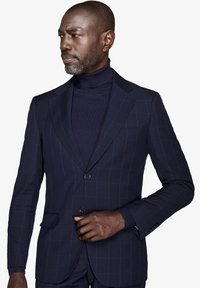 Marineblåternet blazer med en skræddersyet pasform, to knapper og reverslapel. Bæres over en mørk turtleneck med struktureret stof.