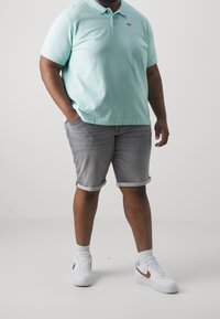 Polo à manches courtes vert menthe, short en jean gris avec ourlets retroussés, et baskets blanches avec des accents dorés. Tenue simple et décontractée.
