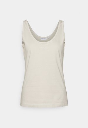 Mouwloze beige tanktop met ronde hals en subtiel merklogo op de borst tegen een effen lichte achtergrond.