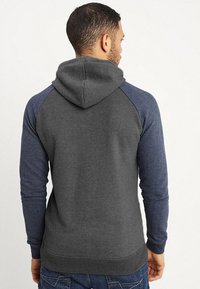 Sudadera gris con un diseño de mangas raglán en azul oscuro. Cuenta con capucha con cordón y puños y dobladillo acanalados, hecha de un material suave.