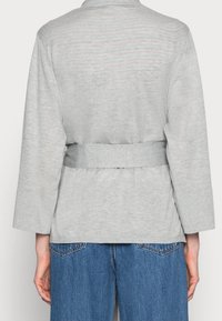 Persona que lleva una camiseta de manga larga gris claro con un cinturón ancho en la cintura, combinada con jeans de mezclilla azul medio de cintura alta.