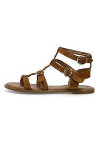 Brune ruskind gladiatorsandaler med flere stropper, sølvfarvede hardware-detaljer, flad sål og åbent tå-design.