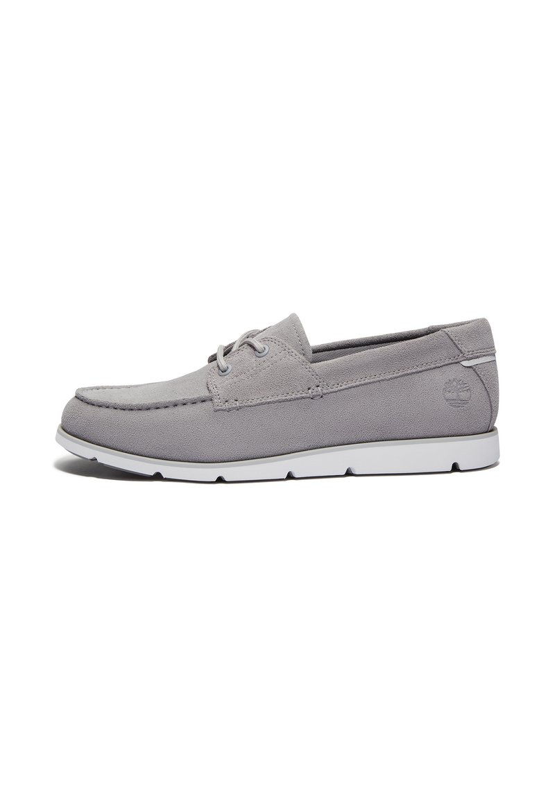 Scarpa da barca in suede grigia con punta tonda, dettaglio di cucitura discreta e suola in gomma bianca. Presenta un design con lacci e logo sul lato.