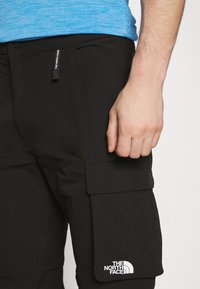 Svarta cargobyxor med en stor sidficka och vitt logo. Tillverkade av lättviktig tyg, med en subtil textur och bältesöglor.