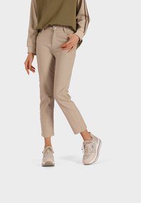 Jeans attillati beige in tessuto testurizzato, abbinati a sneakers beige e grigie con lacci e loghi. L'outfit ha un design rilassato.