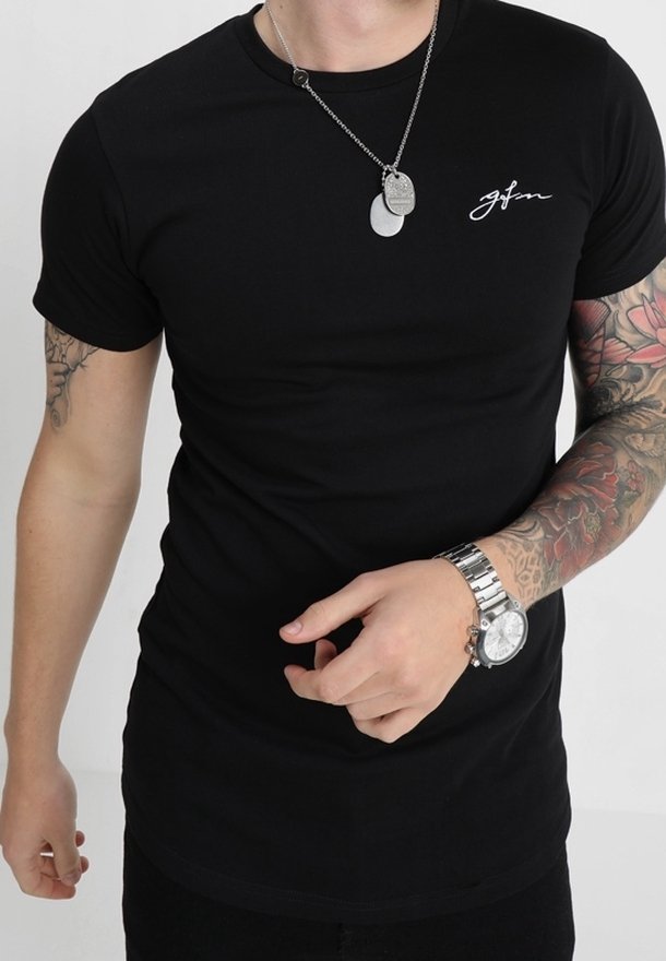 Homme portant un t-shirt noir ajusté avec un petit logo blanc, une chaîne en argent avec des plaques d'identité, une montre en argent et un tatouage floral sur tout le bras droit.