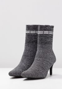 Bottines tricotées en gris et noir avec un bout pointu, un dessus texturé, un poignet côtelé et un fin talon haut. Comprend des rayures blanches en accent.