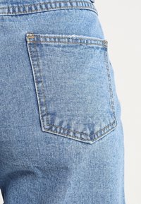 Světle modré džíny mají zadní kapsu s vyztuženým švem a jemnou texturou, což podtrhuje klasický design s pěti kapsami.