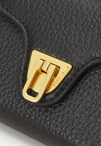 Black textured leather bag featuring a gold-toned triangular clasp with a prominent latch and branded engraving on the side.