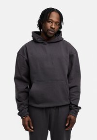 Dunkelgrauer Hoodie mit Kängurutasche, aus strukturiertem Stoff und mit einer Kordelzugkapuze. Weicher, lockerer Schnitt mit Rippbündchen. Passende Hose sichtbar.