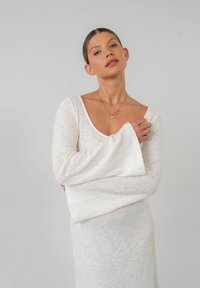Lange mouw witte gebreide jurk met een ronde hals, gemaakt van een textuurstof en met een getailleerd silhouette dat het lichaam bescheiden omarmt.