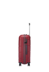 Maleta rígida roja con superficie texturada, varias ranuras horizontales, un asa retráctil y cuatro ruedas para mayor movilidad.