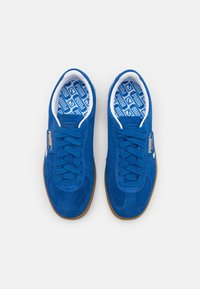 Paire de baskets en daim bleu Puma avec des lacets bleus et des semelles marron, vue de dessus sur fond blanc.