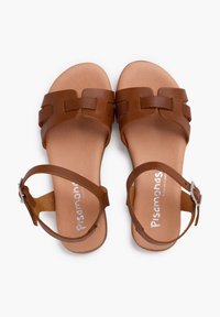 Pruunist nahast sandaalid, millel on laiad ristuvad rihmad ja säärelingi pandla. Sile tallaosa ja lame põhi, sisetallas on reljeefne logo.