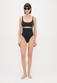 Čierne plavky s hranatým výstrihom, vyrezanými bokmi a detailmi v podobe cik-cak šitia. Majú vysoký strih nohavičiek a sú vyrobené z elastickej tkaniny.