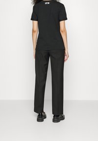 Camiseta de algodón negra con mangas enrolladas combinada con pantalones negros holgados y zapatos negros gruesos, vista desde atrás.