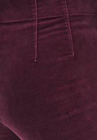 Bordowy materiał kordowy o miękkiej fakturze, z przednimi kieszeniami i średnim stanem. Widoczne szwy i szwy.