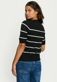 Črni pulover s kratkimi rokavi z belimi vodoravnimi črtami, rebrastim izrezom in robom. Model nosi svetlo modre kavbojke.