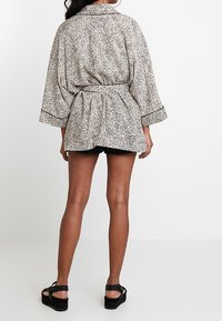 Capa estilo kimono en tela ligera con un estampado de animal en blanco y negro, que incluye un cinturón, mangas anchas y un ribete en contraste.