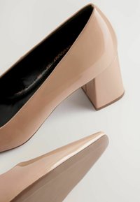 Beige patentoide korkokengät, joissa on paksu lohkare, pyöreä kärki ja sileä pinta. Musta sisävuori näkyvissä.