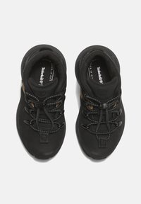 Černé tenisky s hladkým svrškem, elastickými tkaničkami a gumovou podrážkou. Uvnitř boty se nachází logo Timberland.