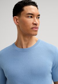 Maglione azzurro chiaro lavorato a maglia con scollo rotondo, maniche corte e una finitura testurizzata. Tessuto liscio con un leggero motivo uniforme.