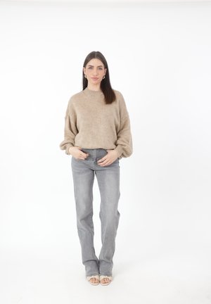 Beige gebreide trui met een hoge nek, ballonmouwen, gecombineerd met lichtgrijze straight-leg jeans en lichtgekleurde sandalen.