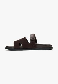 Brown suede sandal featuring two wide straps, an adjustable back strap, and a flat rubber sole with recessed detail.