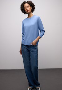 Pull en tricot bleu clair avec un col rond, des manches longues et des poignets côtelés, associé à un jean large bleu foncé. Texture lisse, coupe décontractée.