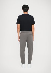 Herrenoutfit mit einem schwarzen kurzärmeligen Hemd und grauen, schmal zulaufenden Sweatpants mit Taschen, vervollständigt mit weißen Sneakers. Glatte Stofftextur.