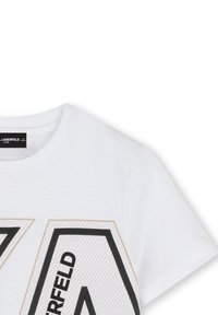 T-shirt en coton blanc avec un grand design géométrique noir et doré sur le devant, un col rond et des manches courtes.