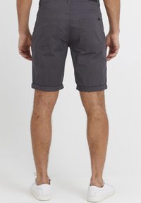 Grå bomullsshorts med rullekanter, med to baklommer og et enkelt design, kombinert med hvite sneakers.