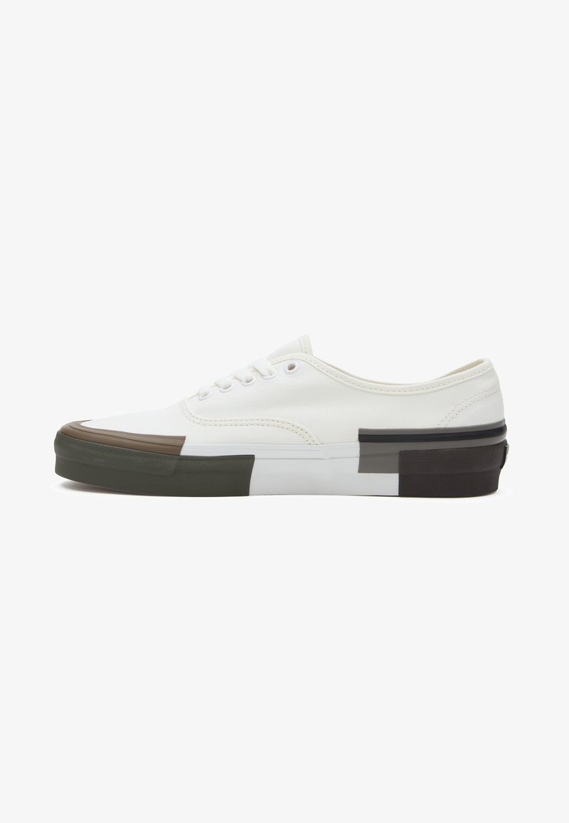 White canvas sneaker with rounded toe, durable rubber sole, and color-block accents in brown, green, and black. Lace-up design with stitching details.