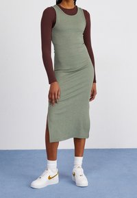 Grön ribbad midiklänning med en åtsittande silhuett, i kombination med en brun långärmad topp. Vita sneakers med guldaccenter fulländar looken.