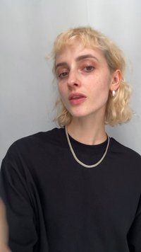 Black t-shirt displayed with a silver mesh necklace and polished silver earrings, featuring a textured finish and round shapes. Light background.