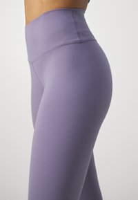 Leggings a vita alta, aderenti, di colore viola chiaro con una texture liscia e cuciture rinforzate per una maggiore durata.