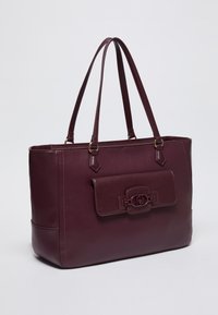 Borsa a tracolla in pelle marrone con due manici lunghi, un accento con patta frontale e una texture sottile. Presenta dettagli in oro e una forma strutturata.
