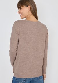 Langärmeliger Pullover aus leicht braunem Strick, mit einem lockeren Schnitt, strukturiertem Finish und rundem Halsausschnitt, kombiniert mit blauen Jeans.