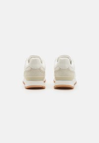 Baskets blanches avec une tige en cuir lisse, des perforations discrètes et un accent en suède beige. Semelle en caoutchouc avec un profil en brun clair.