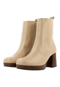 Beige enkellaarzen met een glad leren afwerking, elastische zijpanelen en een houten blokhak. Voorzien van een rits voor gemakkelijk aan- en uittrekken.